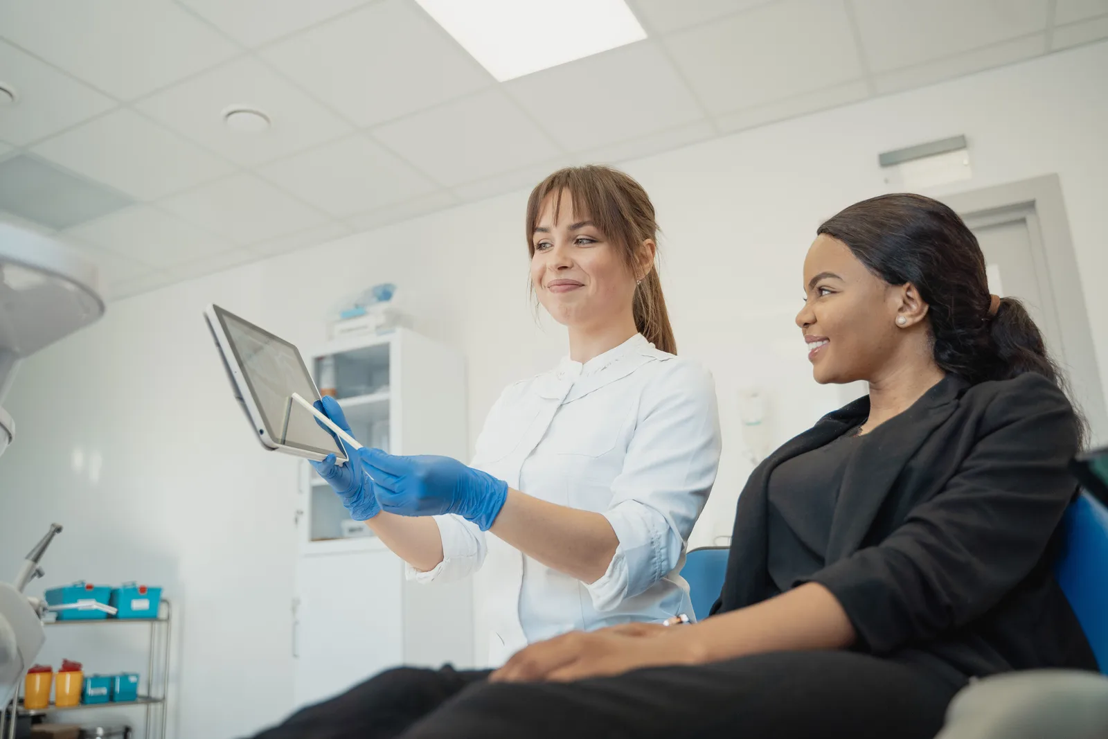 Dentist and patient discussing treatment plan using a tablet in a modern clinic setting. Cost of Dental Marketing in Canada: Planning Ranges
