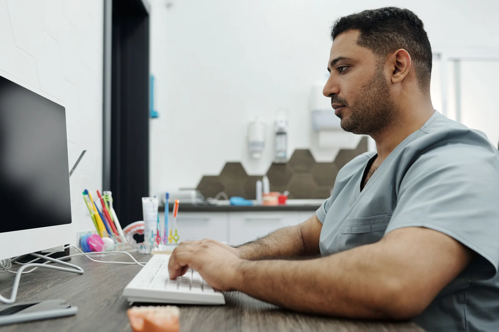 Dentist in scrubs working on a computer at a dental clinic, with focus on patient management. How to evaluate dental advertising options