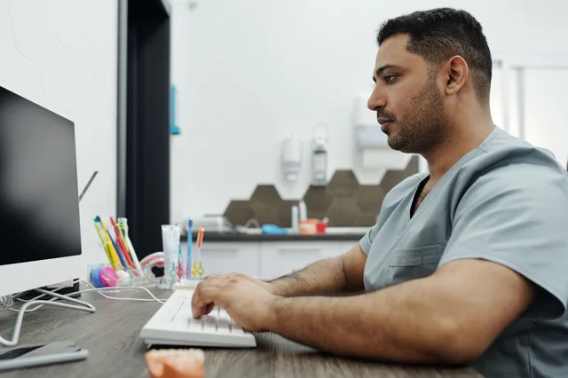 Dentist in scrubs working on a computer at a dental clinic, with focus on patient management. How to evaluate dental advertising options