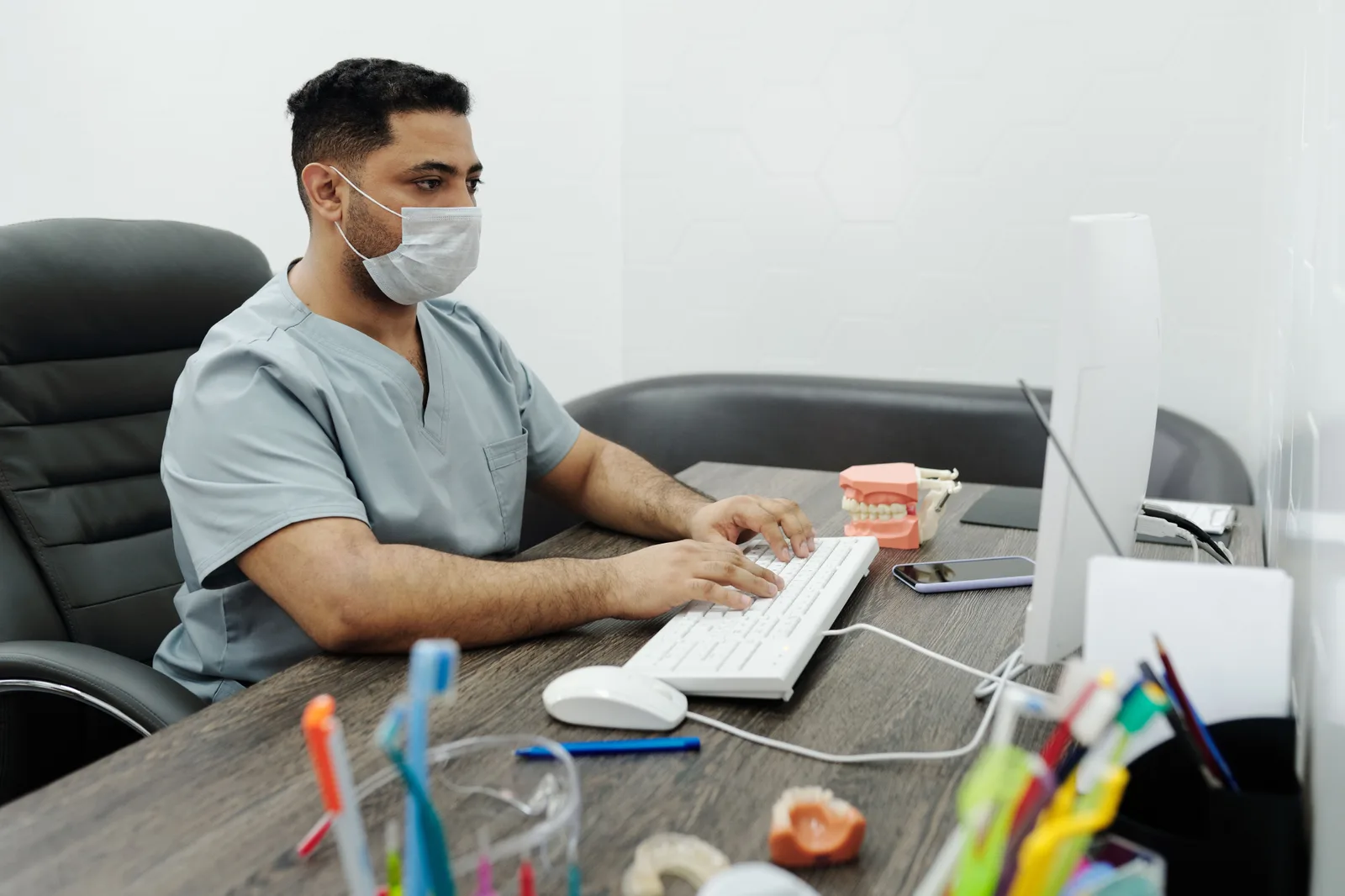 Dentist wearing mask working on computer at office desk with dental model. The dental reputation management trends that will still matter next year