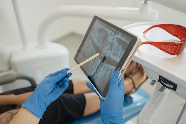Dentist showing dental x-ray on tablet to patient in a modern clinic setting. Can You Remove a False Google Review for a Dental Practice?