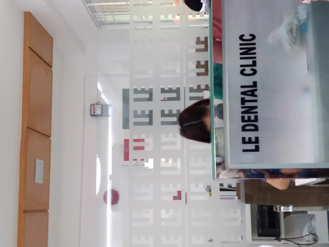 Reception desk at a dental clinic in Imus, Cavite, behind a patterned glass partition and clinic sign.