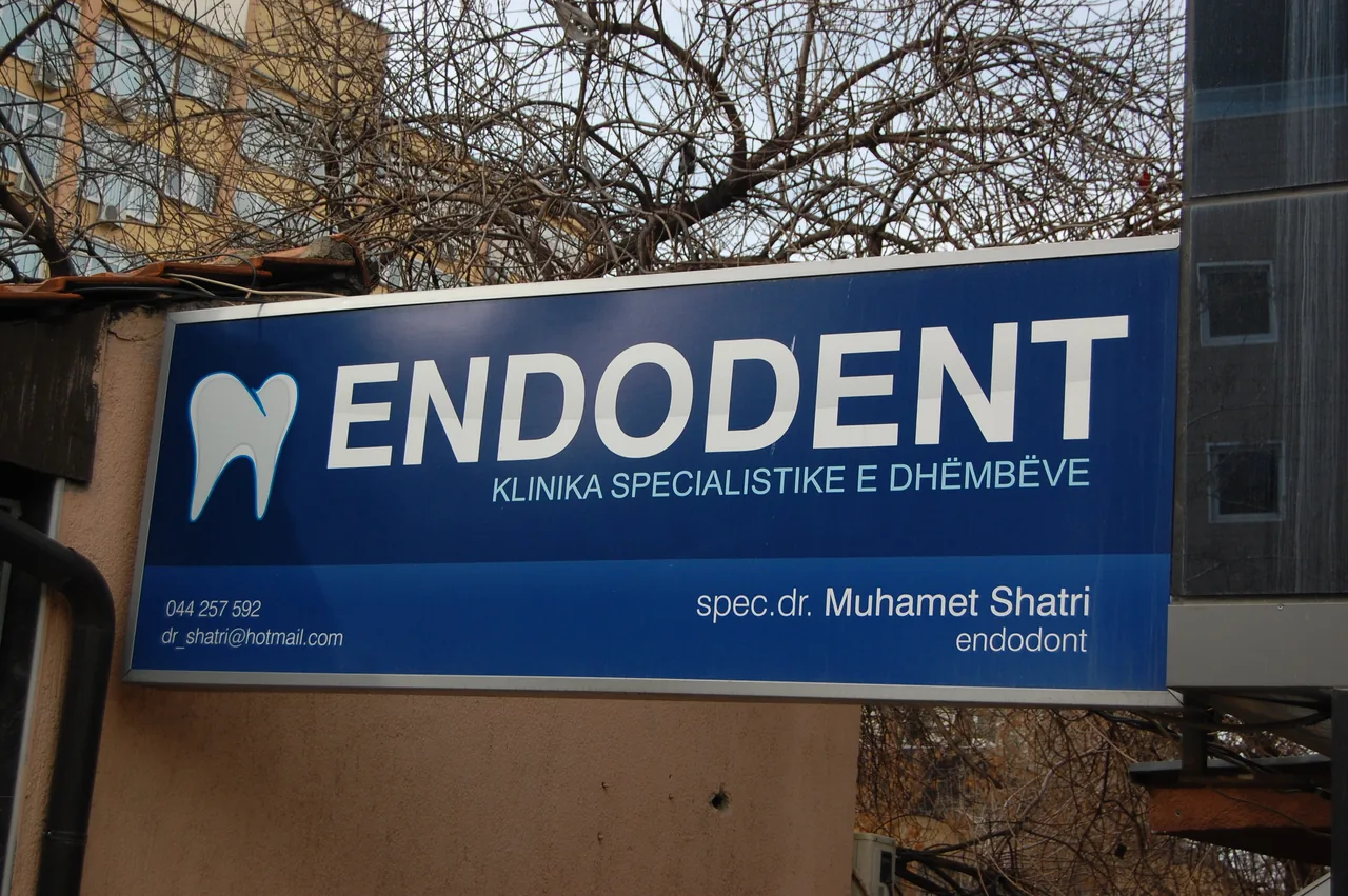 A blue sign identifying a specialist dental clinic in Pristina, Kosovo.