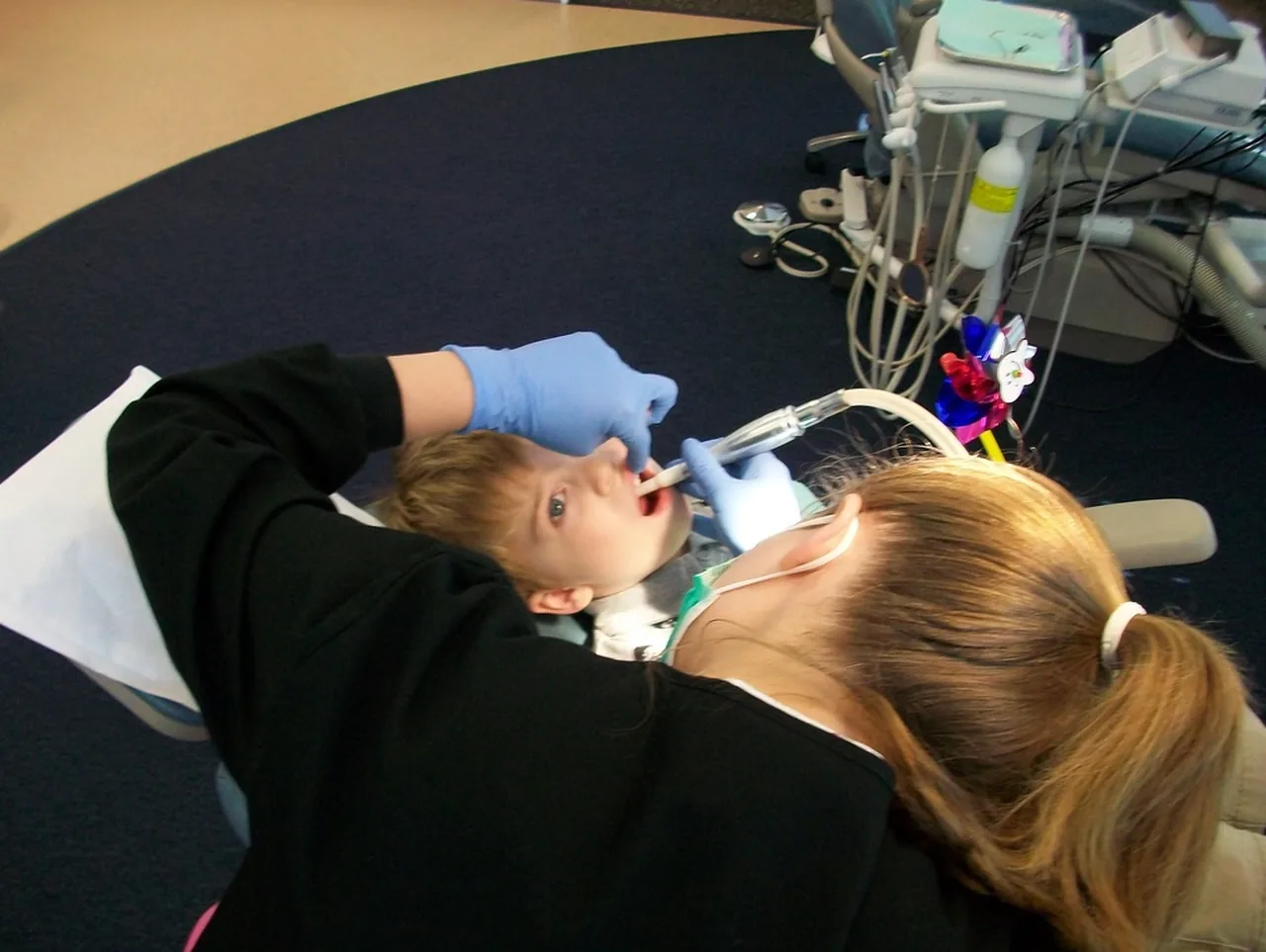 A dentist wearing protective equipment treats a patient in a dental chair.